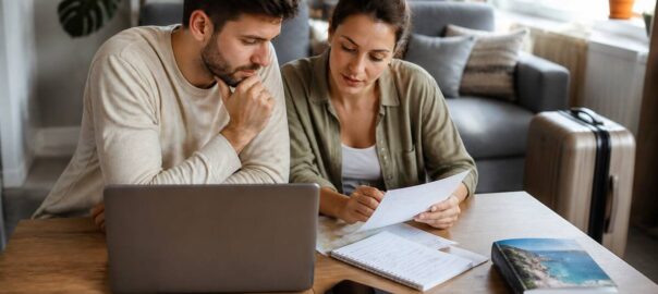 Een stel vergelijkt reisopties op een laptop en met papieren notities, in een gezellige woonkamer